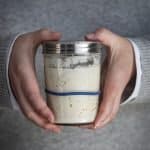 Two hands holding a glass jar with sourdough starter in it