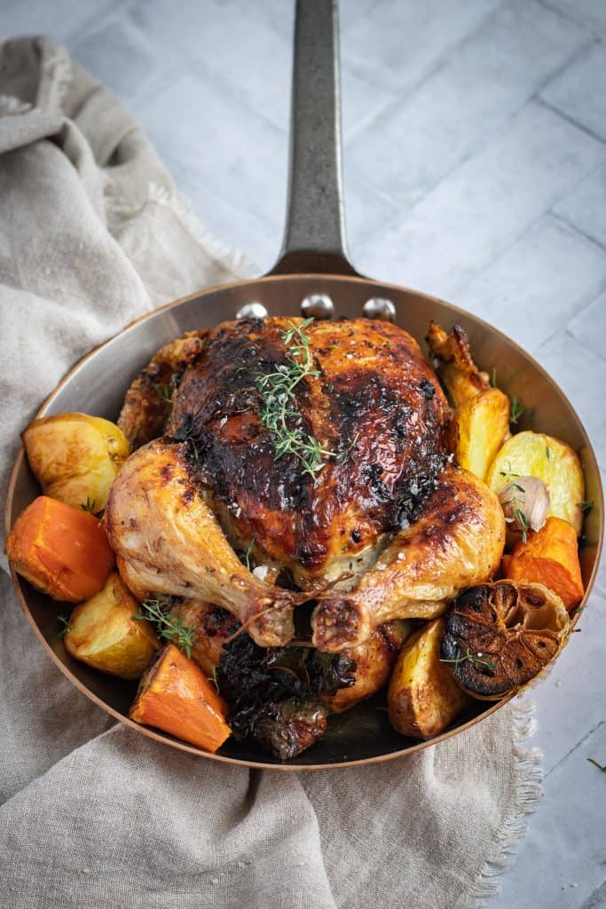 black garlic butter roast chicken in a copper pan with roasted root vegetables