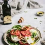 a simple caprese salad on a table with cutlery and a bottle of balsamic vinegar