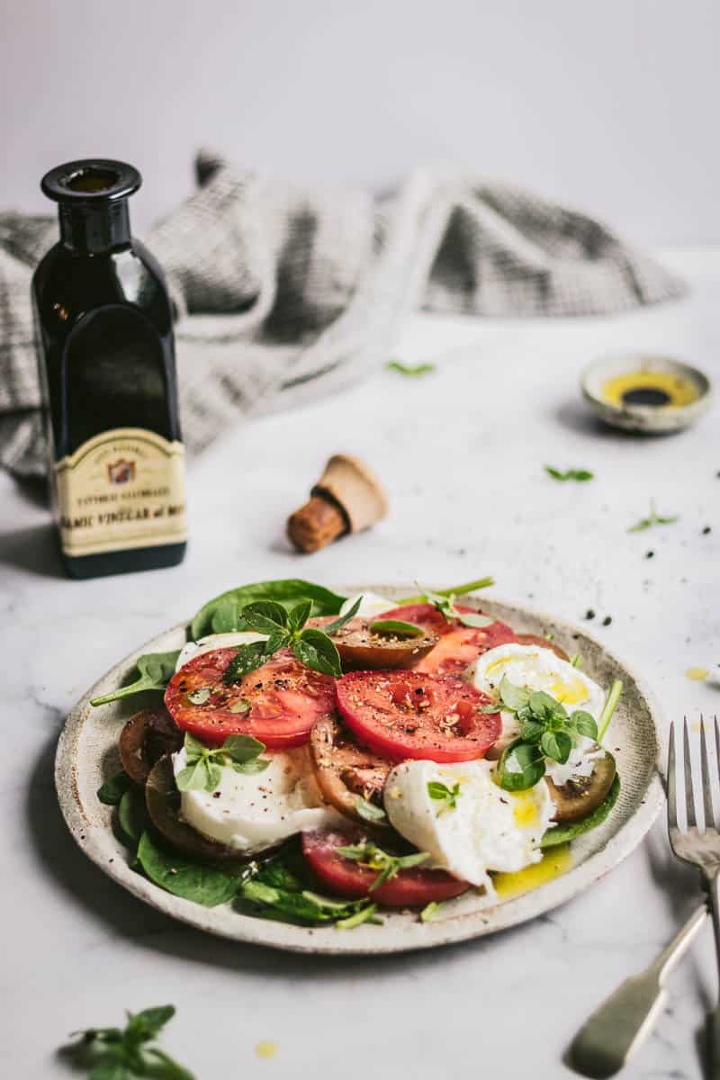 A simple caprese salad on a table with a bottle of balsamic and cutlery