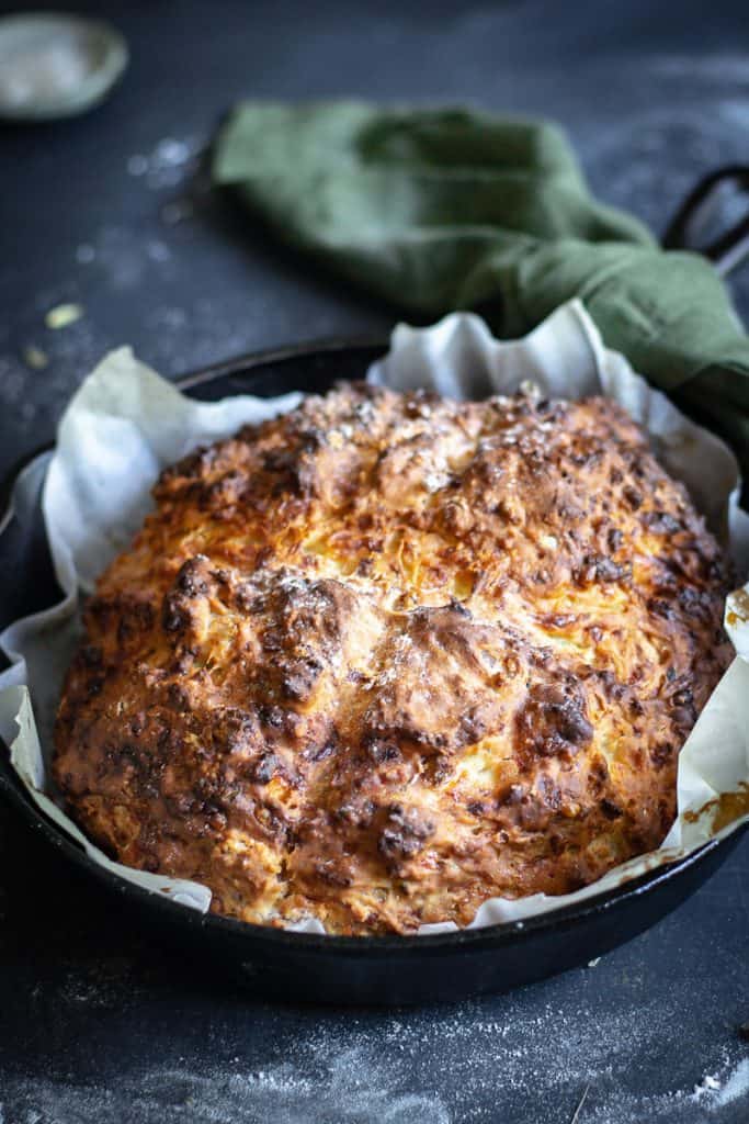 a loaf of Irish cheddar soda bread in a cast iron frypan just out of the oven on a floured table.