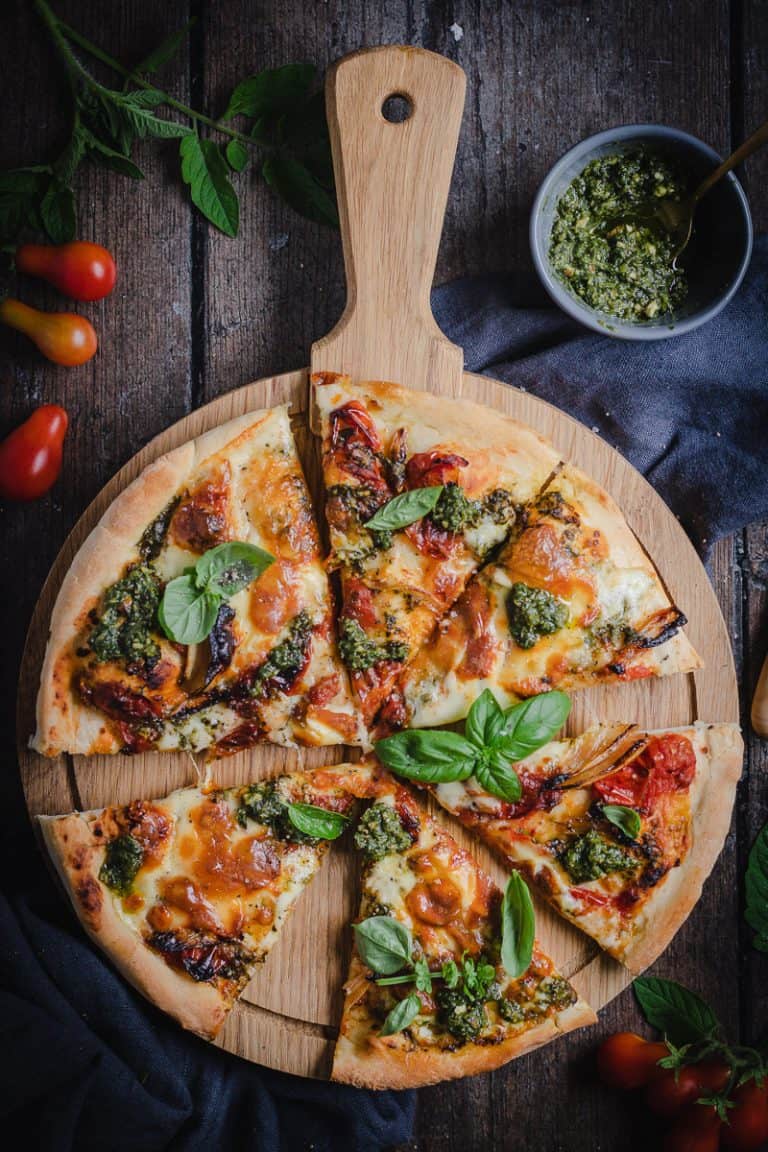 a pesto and slow roasted tomato pizza on a round pizza board on a table