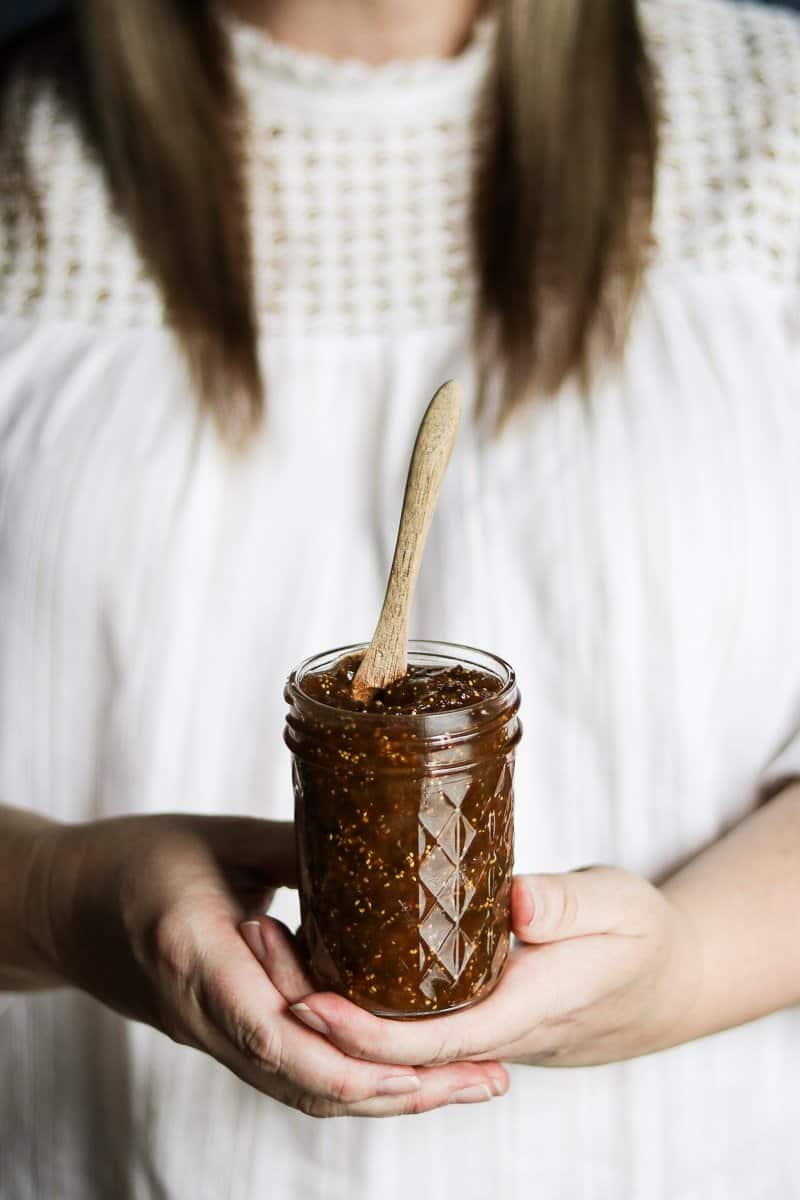 A woman holding a jar of balsamic fig jam with both hands.