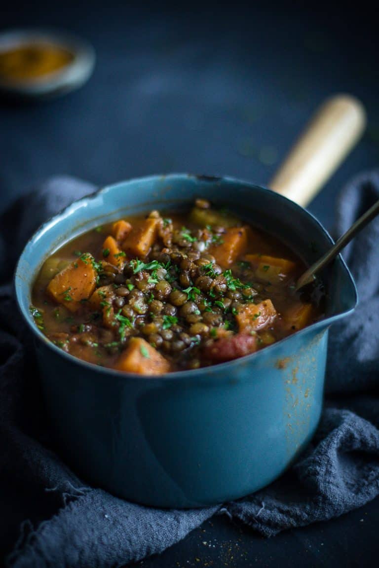 A enamel saucepan full of Persian lentil sweet potato soup with a spoon in it.
