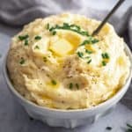 a bowl piled high of creamy mashed potato with a dob of butter on top and finished with a sprinkle of chives