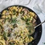 cast iron frypan full of creamy pesto chicken tortellini with a spoonful eaten out of it.