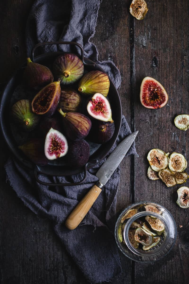 Slicing fresh figs on a timber table alongside a jar of fig slices already dehydrated.