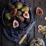 a tray of whole figs being cut, ready for dehydrating. A jar sits in the corner full of sliced dehydrated figs