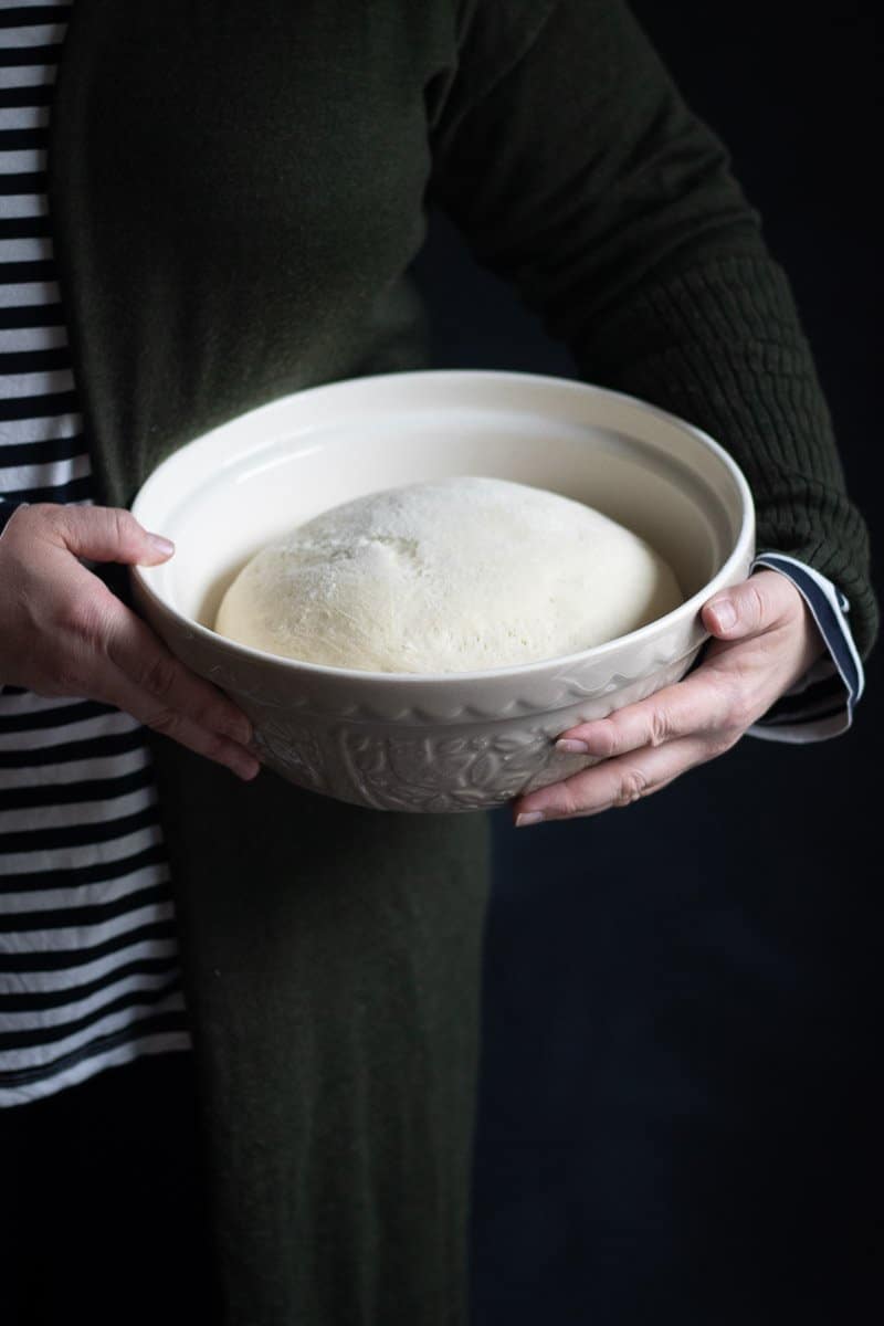 a person holding a bowl of prooved pizza dough in a mixing bowl.