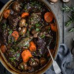 a oval cast iron french oven full of slow cooked beef cheeks in red wine with carrots and mushrooms.