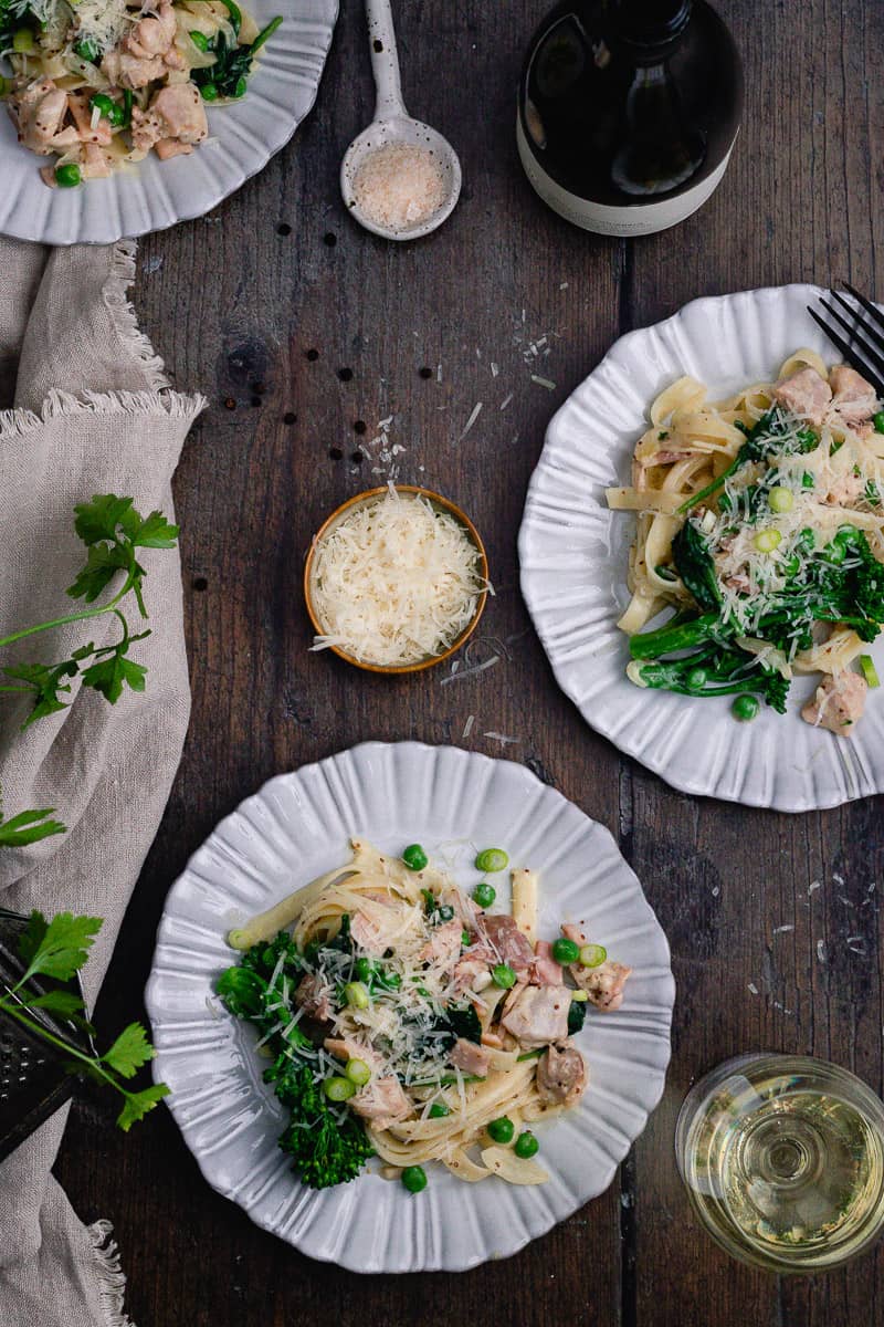 three plates of fettucine boscaiola on a table with wine and grated parmesan