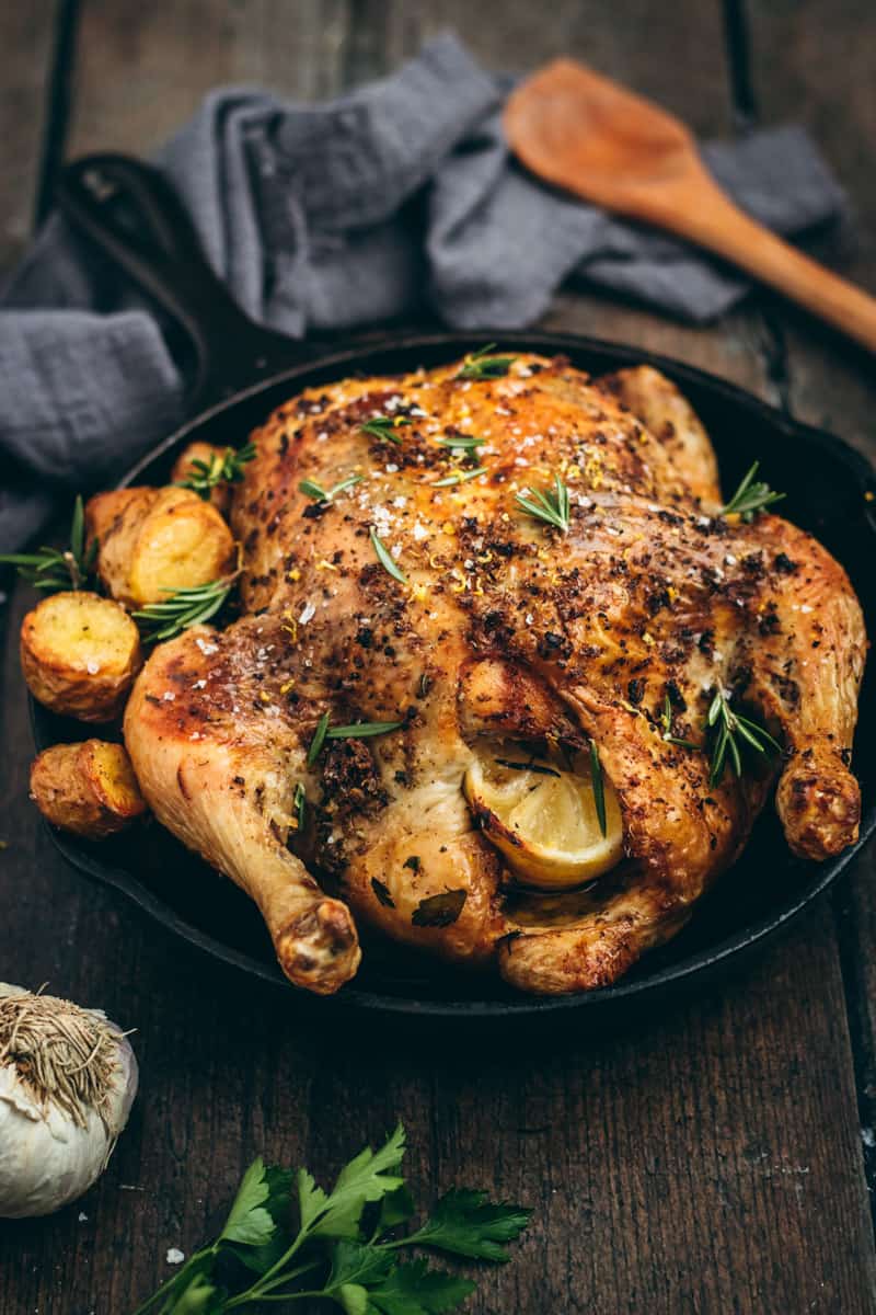 a black cast iron pan with a Greek style whole roast chicken and roast potatoes. 