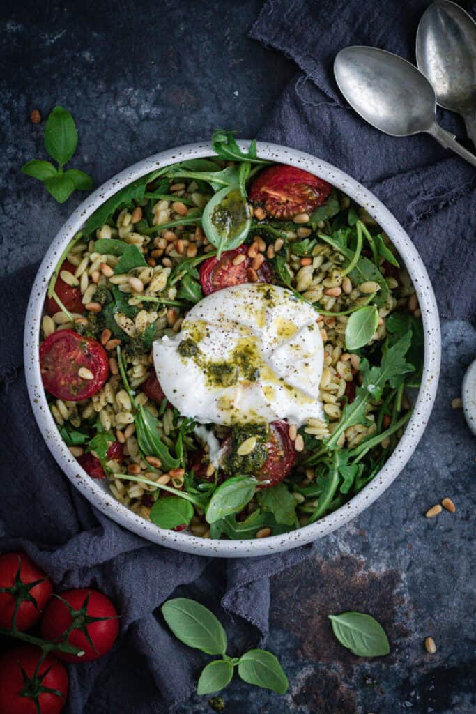 a bowl of pesto orzo salad with a whole burrata drizzles with pesto and extra virgin olive oil on top