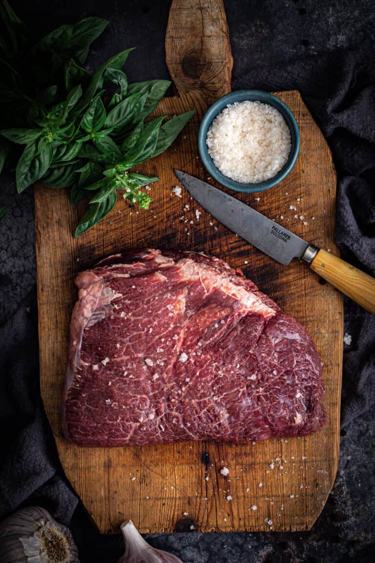 a beef cheek sprinkled with sea salt flakes, sits in a chopping board ready for cooking