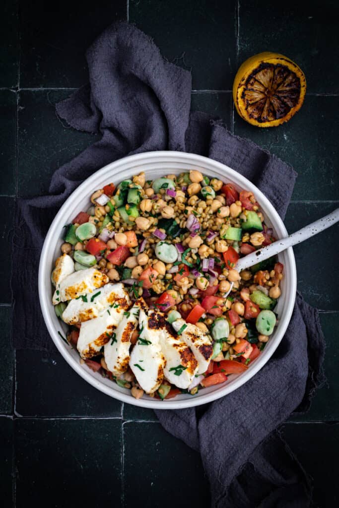 A Bowl of Freekah, fava bean and chickpea salad with sliced halloumi on top