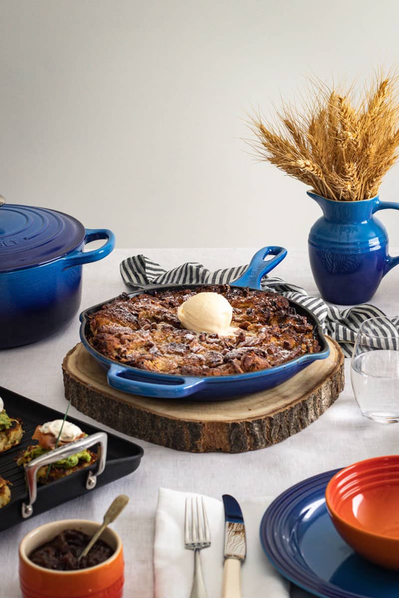 A baked apple french toast in a blue cast iron frypan on a set table of other blue and orange cookware pieces.