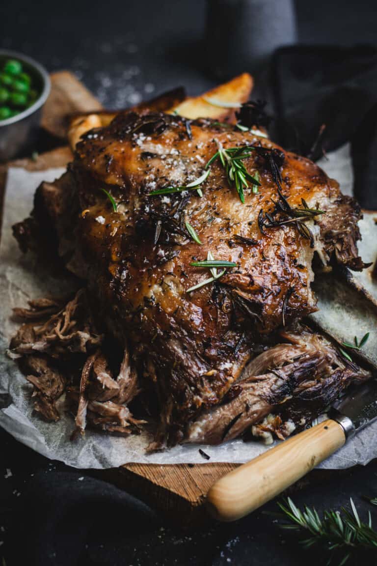 A Slow-cooked lamb shoulder with some of the meat pulled apart on a timber chopping board.