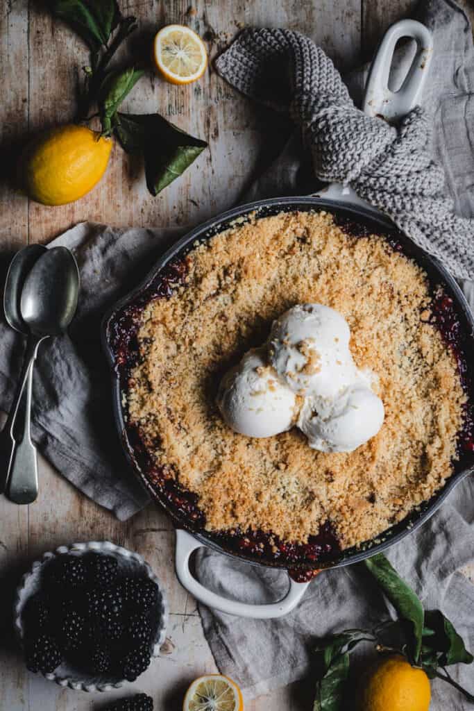 a cooked apple and blackberry crumble in a cast iron skillet topped with scoops of vanilla ice cream.