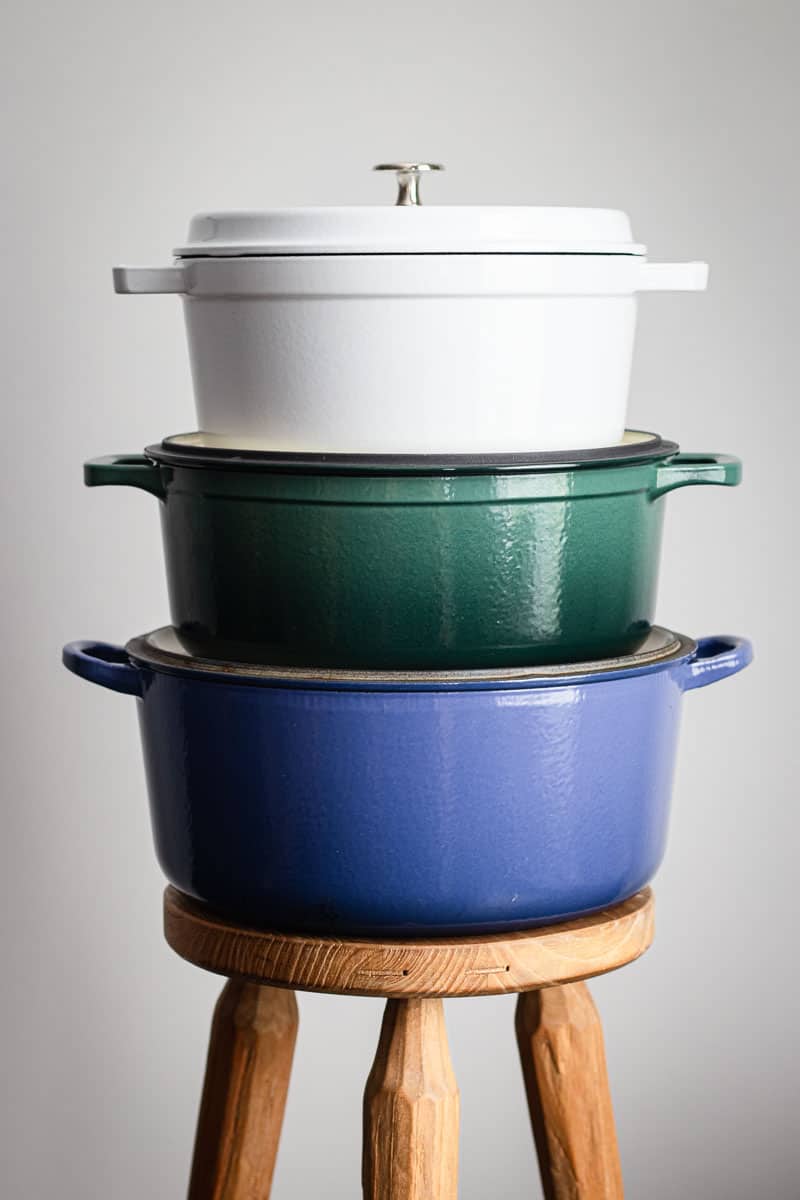 A stack of three colored enamel Dutch ovens on a timber milking stool.