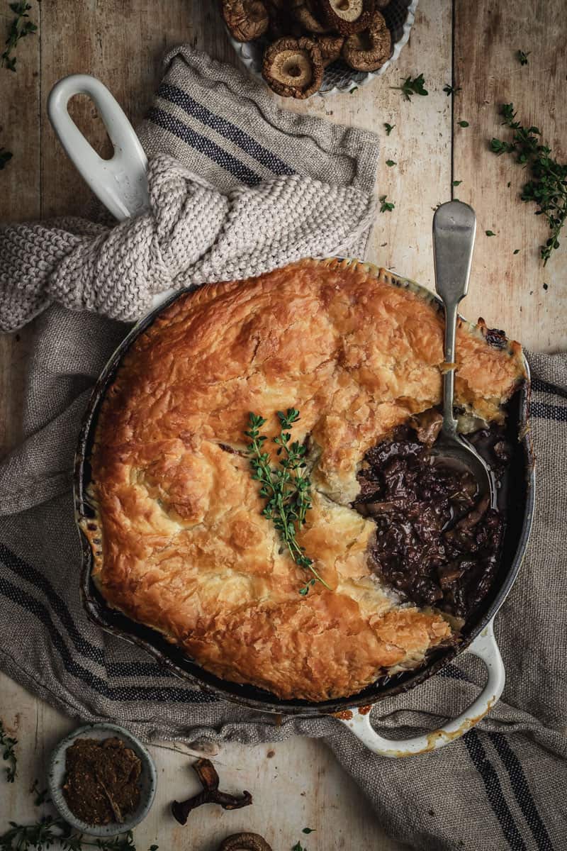 Beef cheek bourguignon pie in a skillet with a scoop taken out and eaten. 