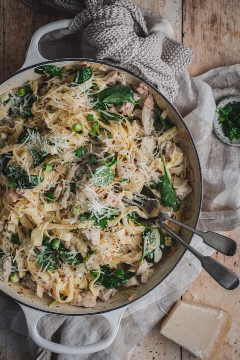 A white cast iron shallow casserole of fettuccine boscaiola finished with shallots, English spinach and parmesan.