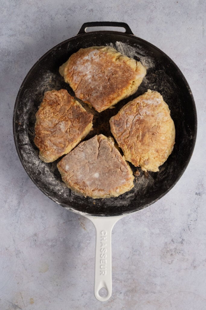 A floured cast iron pan with golden Irish soda farls cooked in it. 