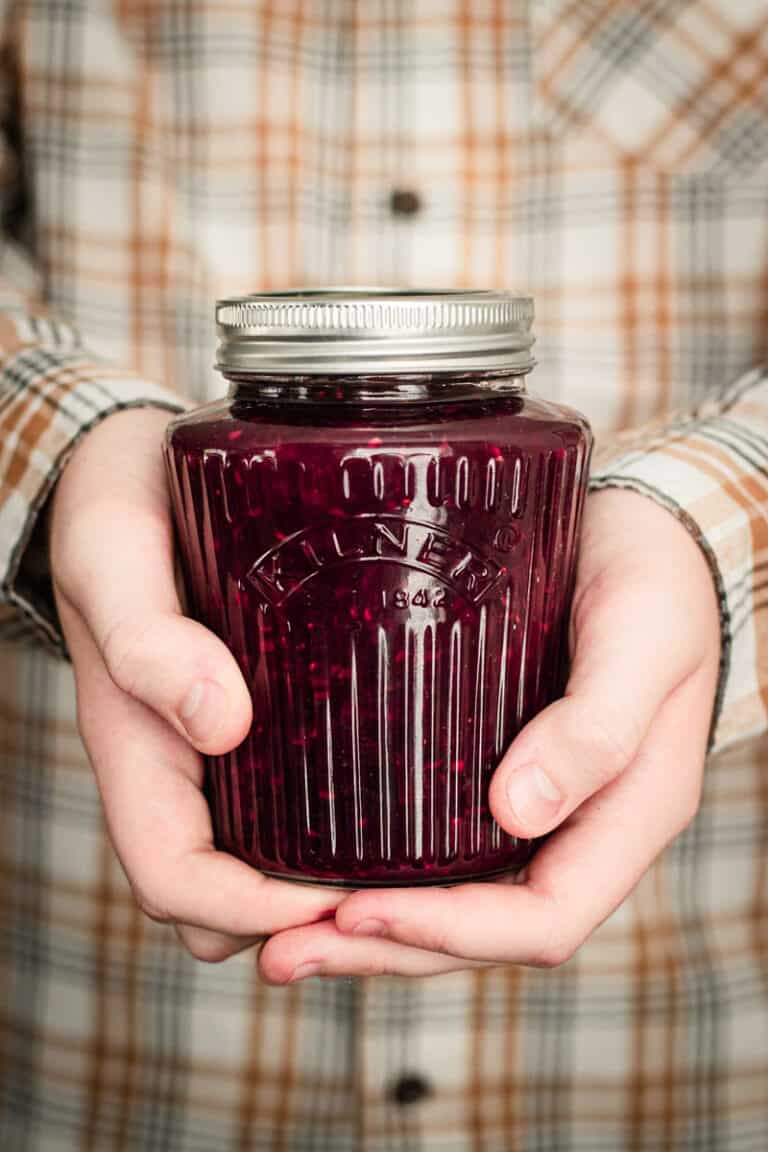 A boy holding a jar of three berry jam with both hands.
