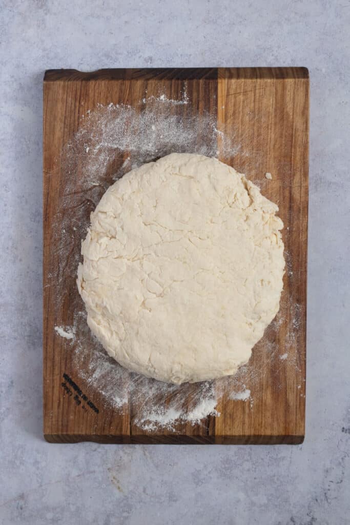 The dough is in a round ball on a wooden board.